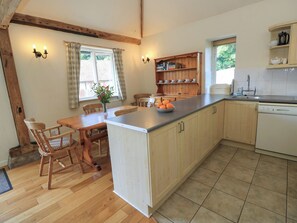 A kitchen with wooden cabinetry, a central island, a dining table with chairs, and a window with curtains.