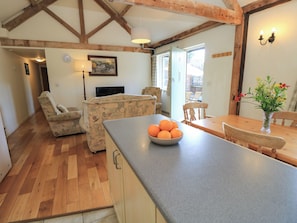 A living room with a sofa, a dining table with chairs, a kitchen area with a countertop, and a wooden ceiling structure. - Byre Cottage 2 (Pulborough)