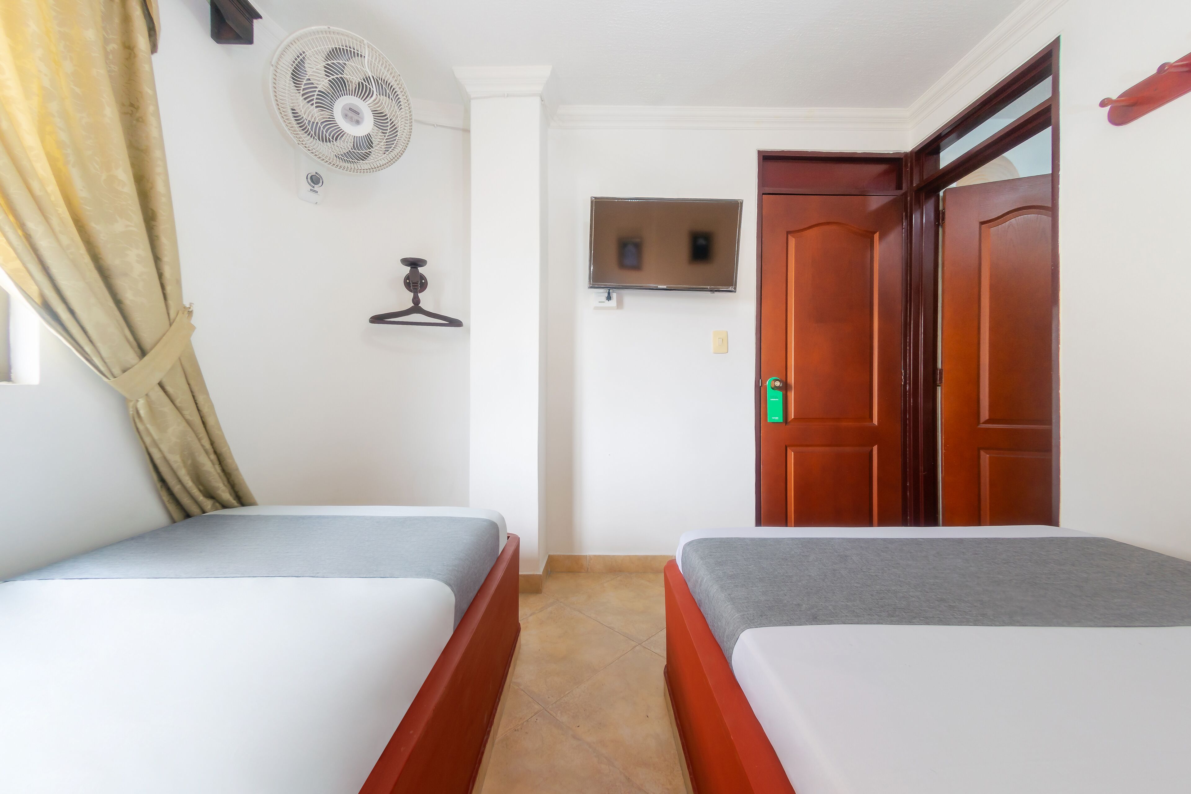 Una habitación con dos camas individuales, un televisor en la pared, una puerta de madera y un ventilador de techo.