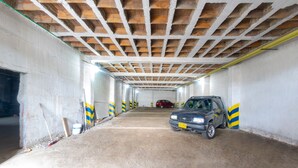 Un estacionamiento con piso de concreto, vigas de madera en el techo y un coche azul estacionado a la derecha.
