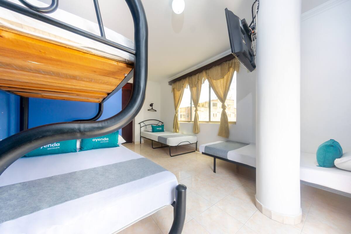 A hotel room with bunk beds, a single bed, a desk, and a window with curtains.