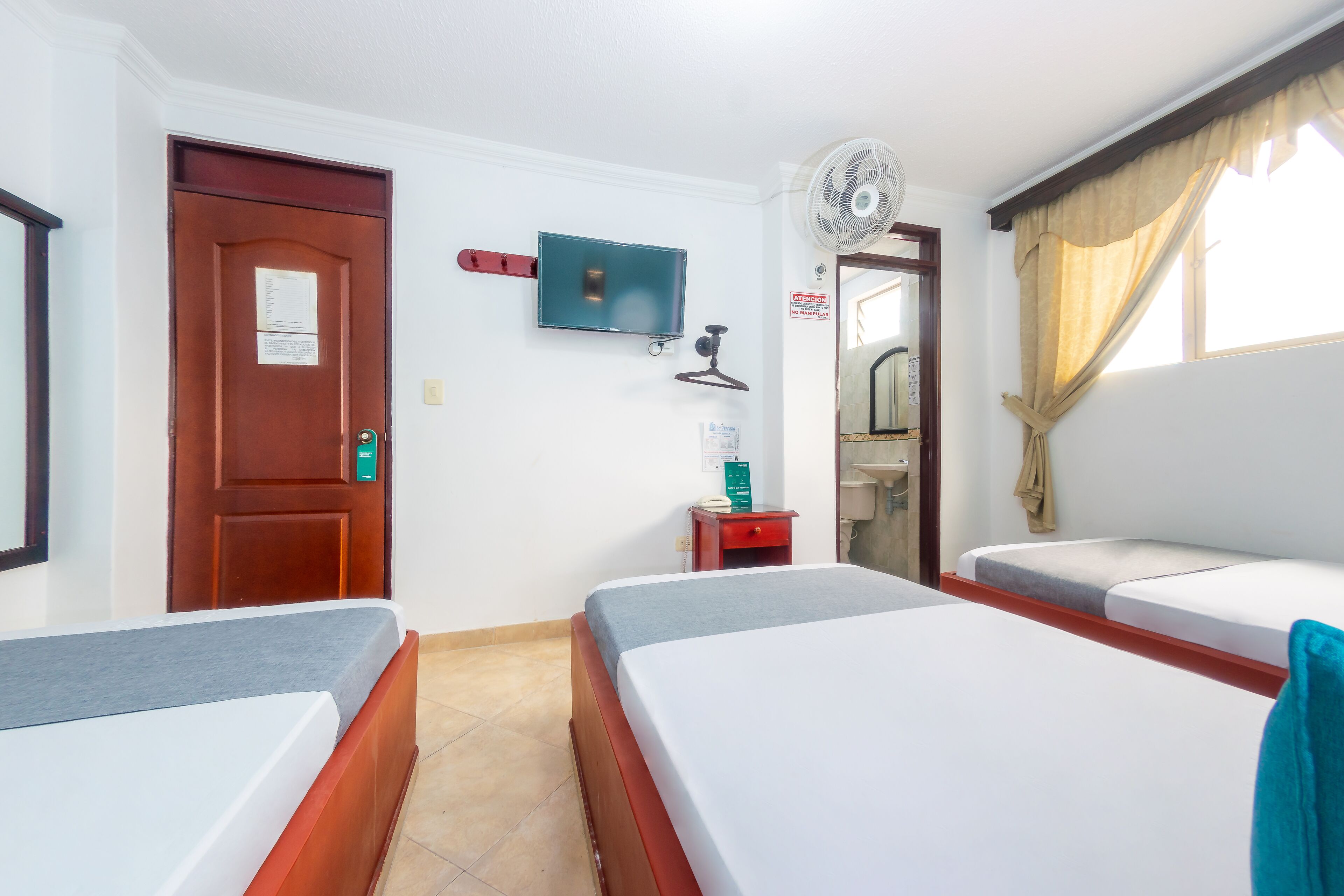 A hotel room with two beds, a TV, a fan, a door, and a window with curtains.