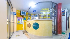 Un área de recepción con un mostrador amarillo, una mesa de recepción y un letrero que dice 'ayenda HOTELS'.