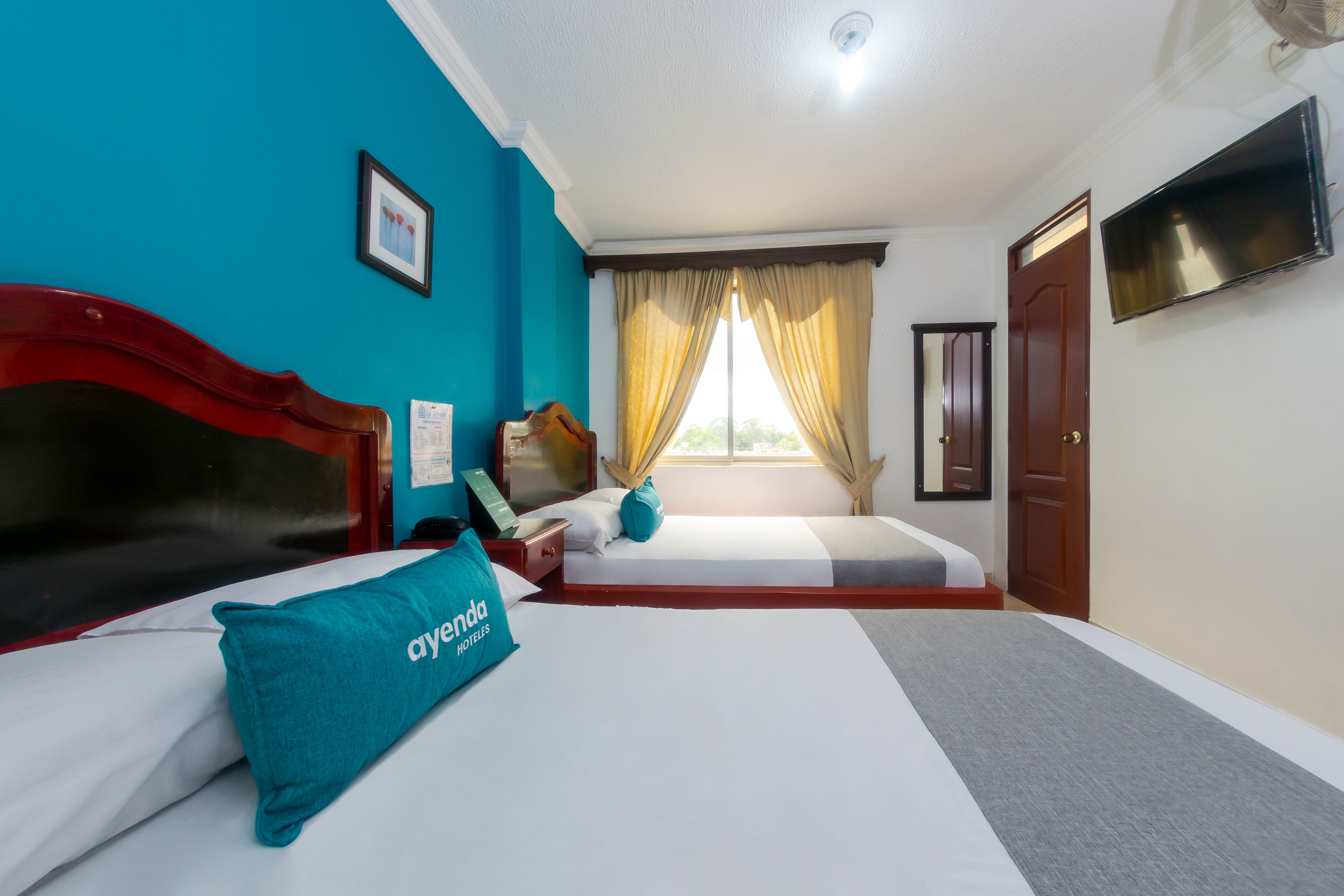 A hotel room with a bed, a desk, a chair, a TV, and a window with curtains.