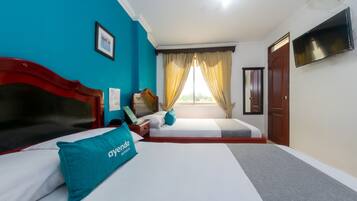 Una habitación de hotel con cama, escritorio, silla, televisor y ventana con cortinas.