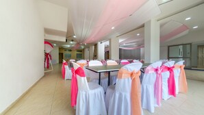Un salón de conferencias con sillas y mesas blancas, cintas rosas y anaranjadas, y un techo alto con tela decorativa.