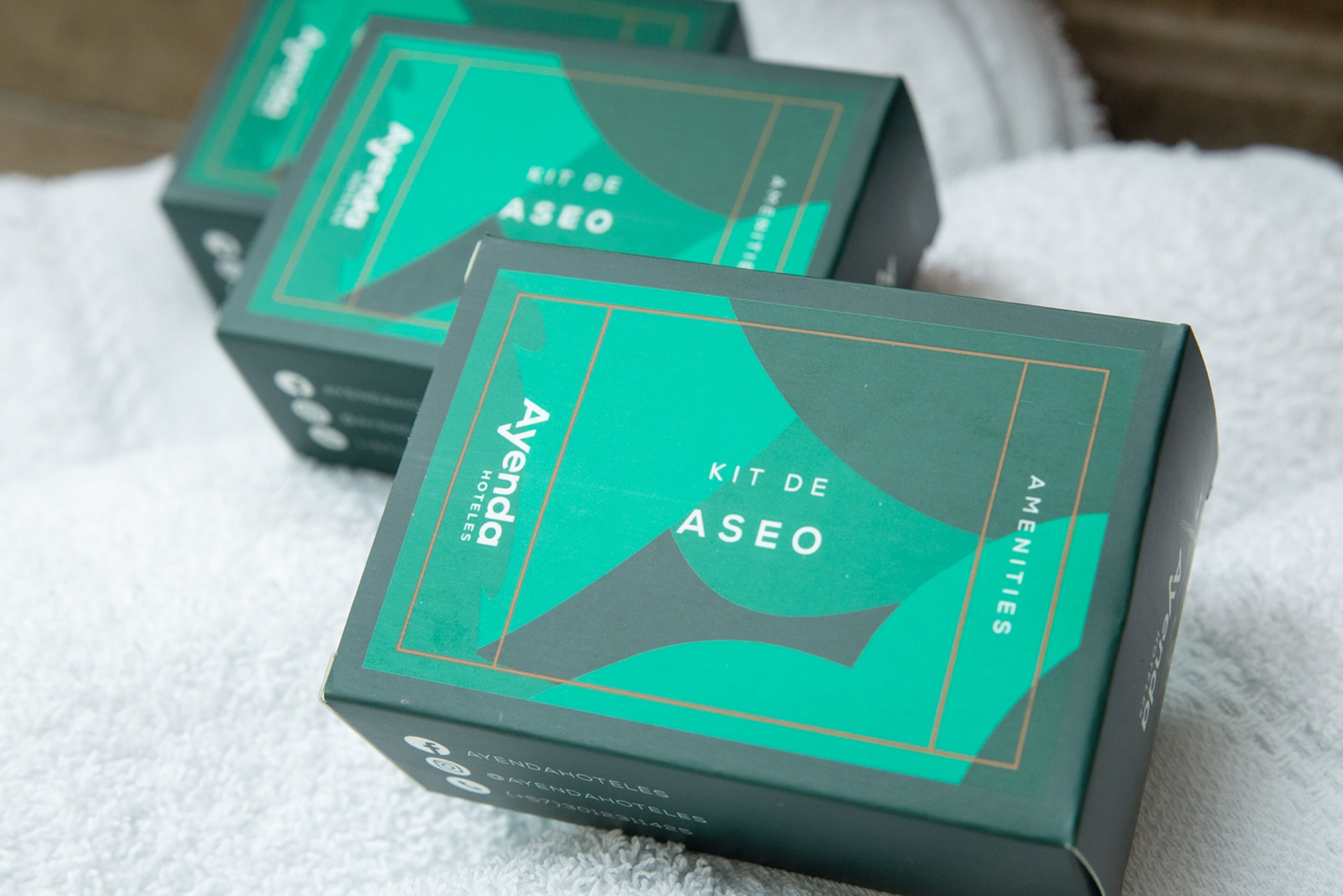 Three green boxes labeled 'Aventura Kit de Aseo' on a white towel.