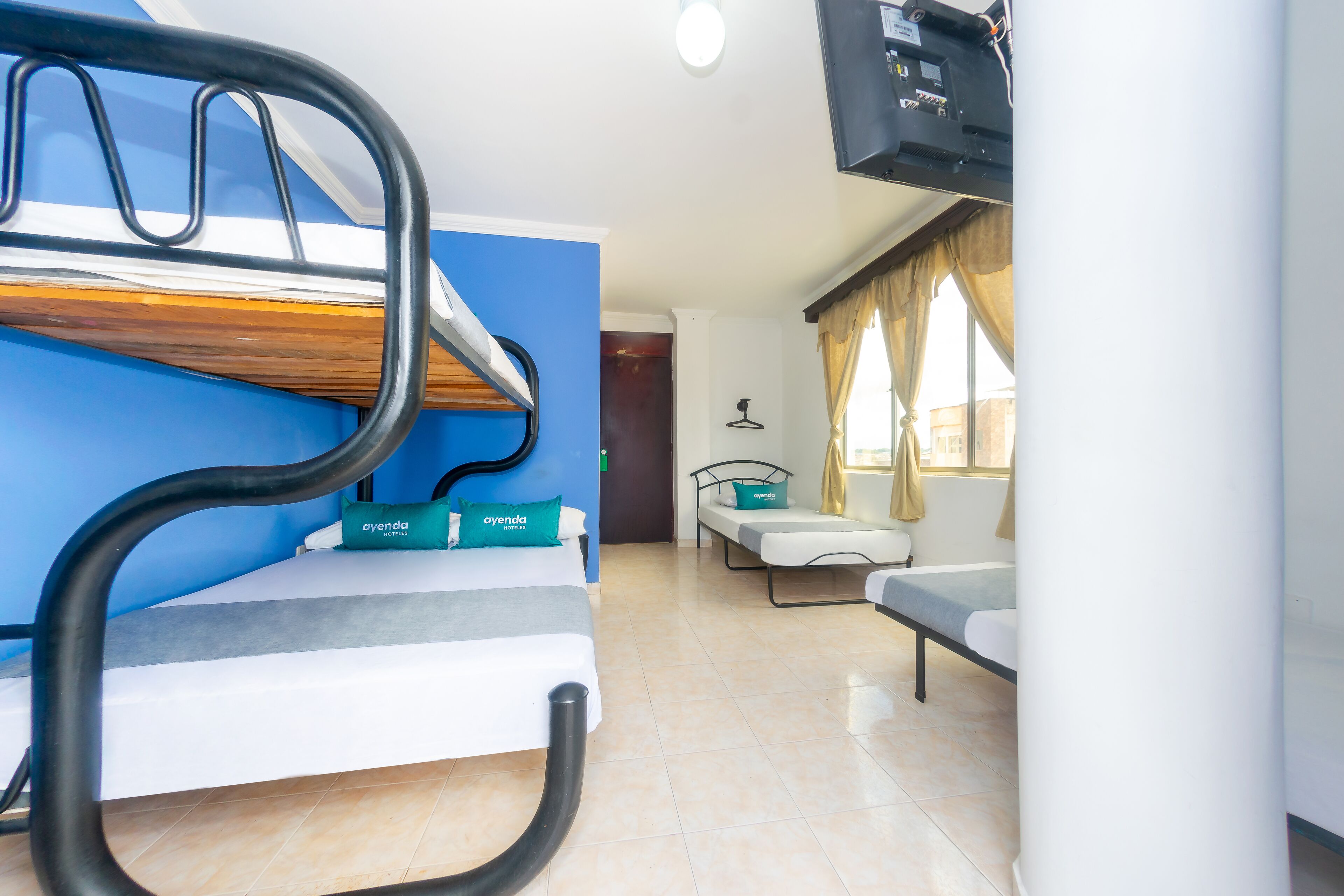 A room with a bunk bed, a sofa, a TV, and a window with curtains.