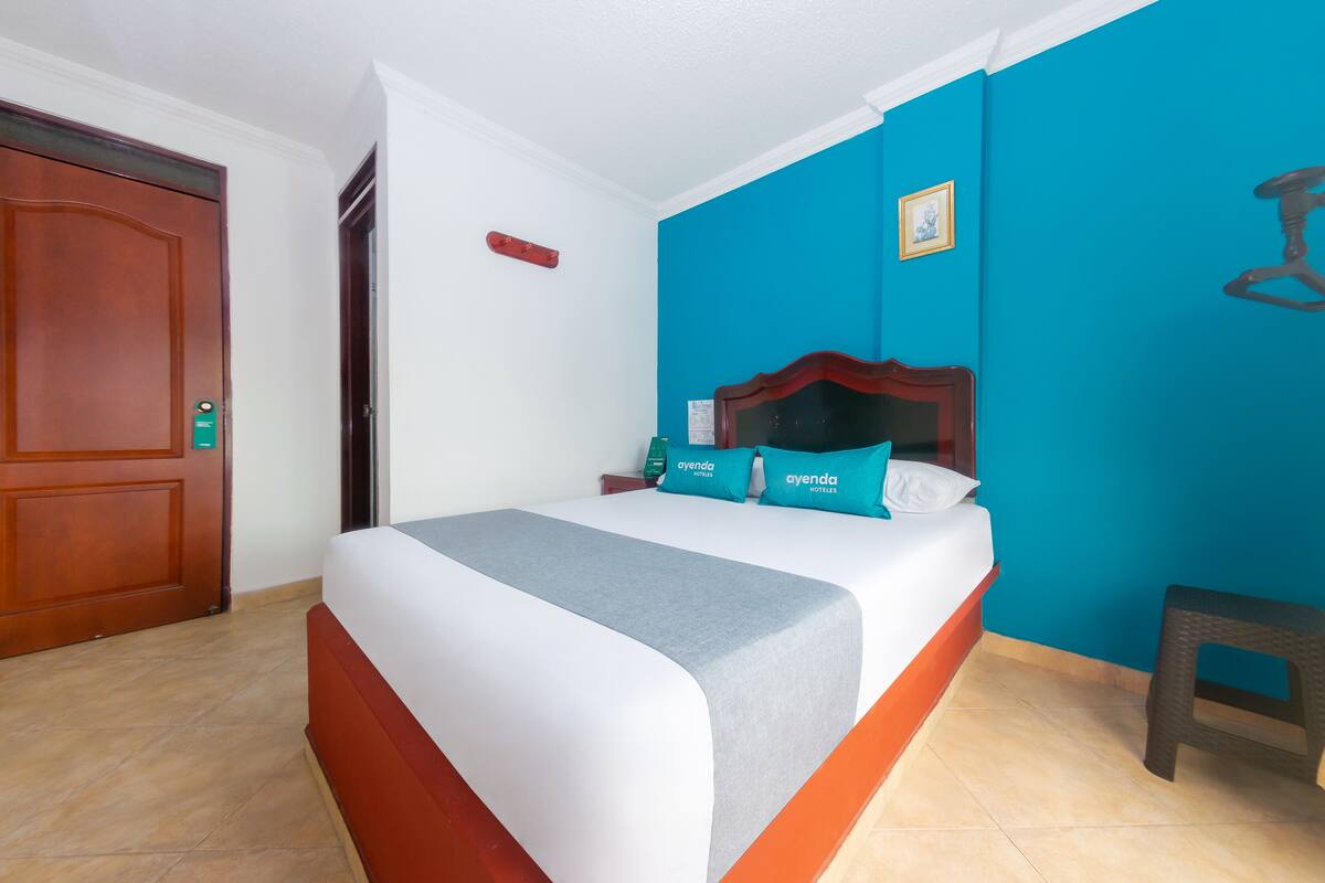 A hotel room with a bed, a nightstand, a wooden door, and a blue accent wall.