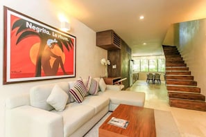 Uma sala de estar moderna com sofá, mesa de centro e escada que dá acesso a um andar superior.