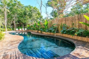 Uma piscina de borda curva, rodeada por vegetação exuberante e um cercado de bambu.