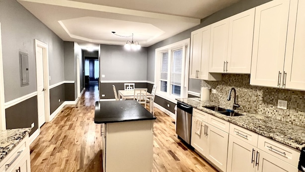 A spacious kitchen with a central island, wooden flooring, and white cabinetry.