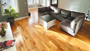 A spacious living room with hardwood flooring, a sectional sofa, a coffee table, and a ceiling fan.