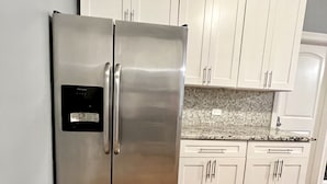 A kitchen with white cabinets, a stainless steel refrigerator, and a patterned backsplash.