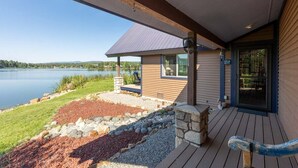 A lakeside property with a wooden deck, stone steps, and a glass door leading to a covered porch.