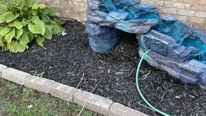 A garden with a brick wall, a green hose, and a plant with broad leaves. - Colorful home near Purdue! (Lafayette)
