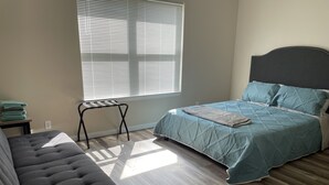A bedroom with a bed, a bench, a window with blinds, and a small table with folded towels. - Colorful home near Purdue! (Lafayette)