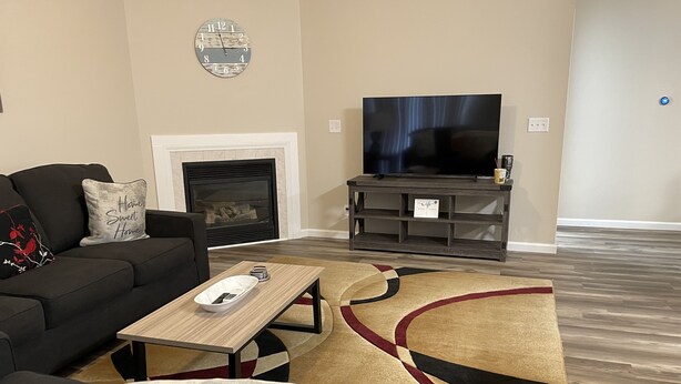 A living room with a black sofa, a coffee table, a TV on a stand, a fireplace, and a patterned rug. - Colorful home near Purdue! (Lafayette)