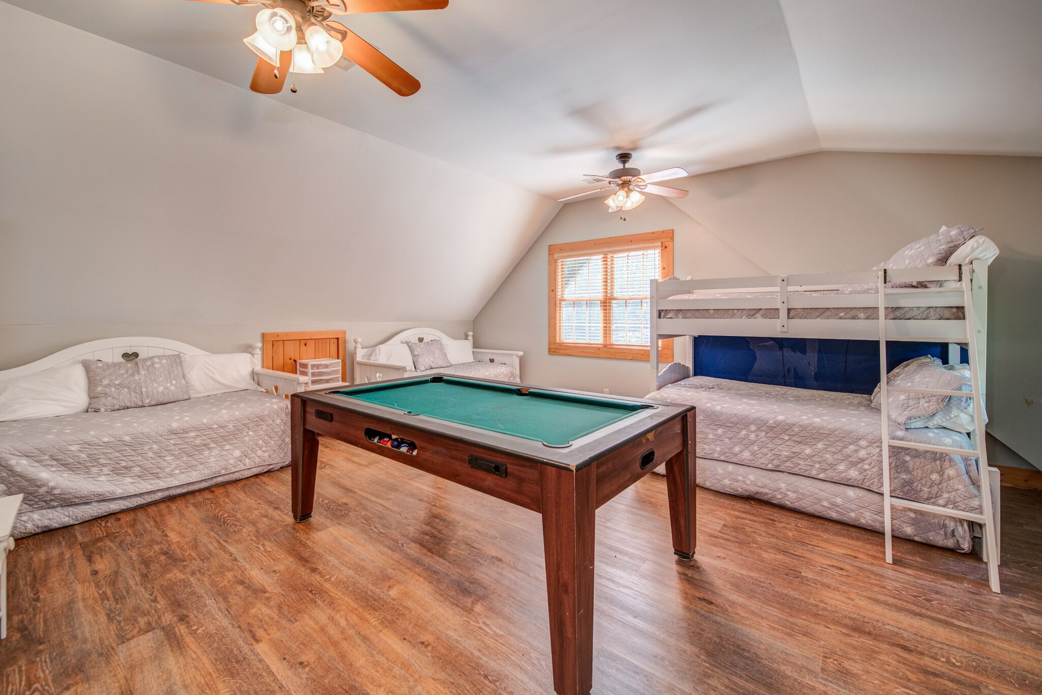 Une pièce avec une table de billard, des lits superposés et un ventilateur de plafond.