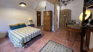 Un dormitorio con cama, mesitas de noche, armario, escritorio con silla y lámpara colgante.