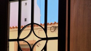 Vista a través de una reja de metal con un diseño decorativo, que da a un edificio con entrada de azulejos y una calle empedrada.