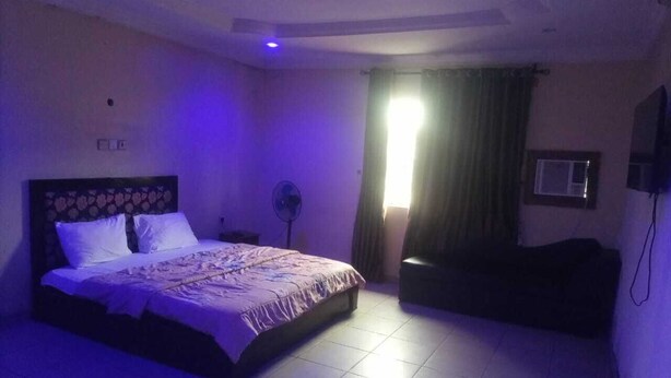 A bedroom with a bed, a fan, a window with curtains, and a wall-mounted TV. - Homewood Suites (Lekki)