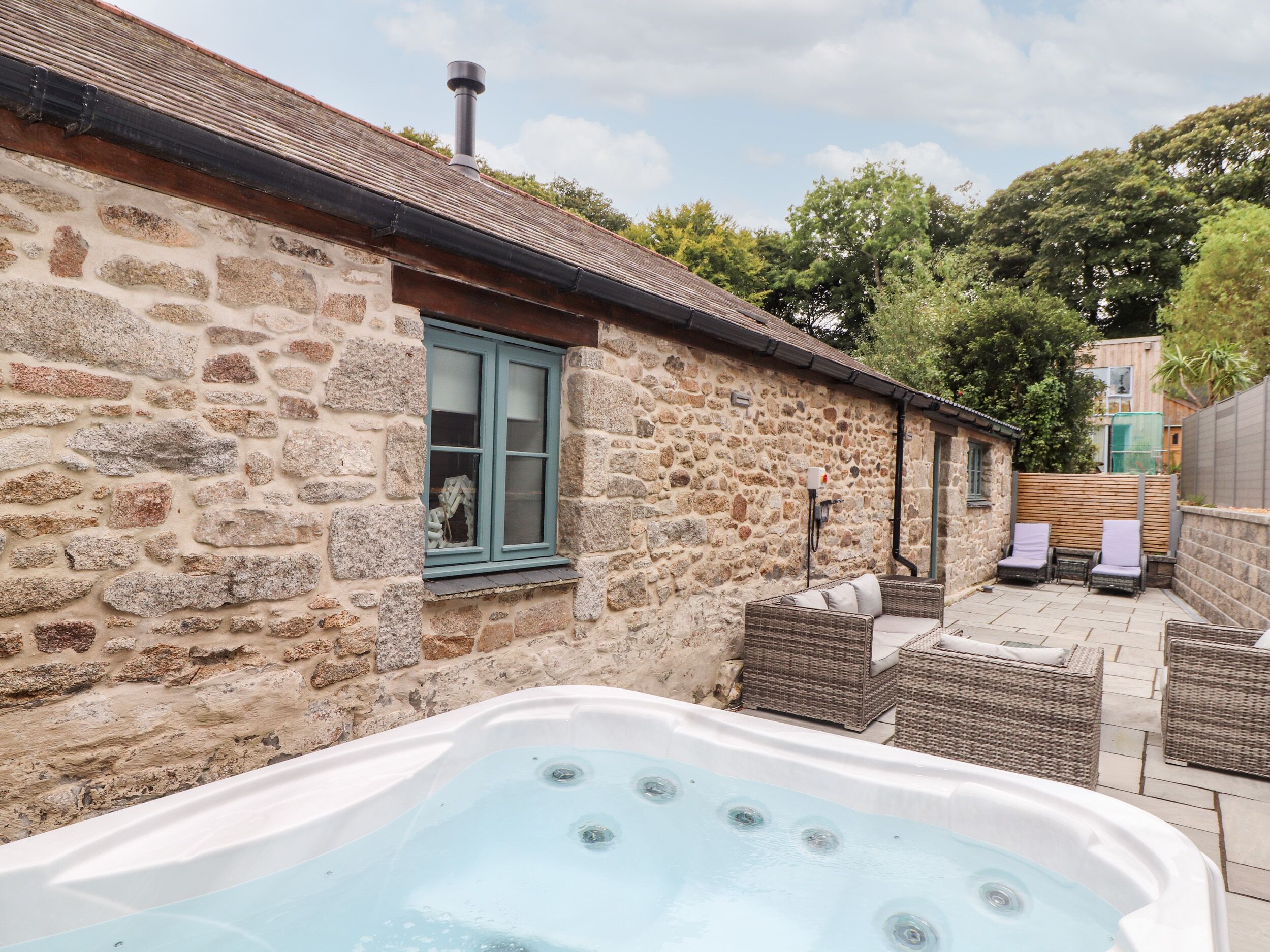 A stone building with a hot tub and wicker furniture.