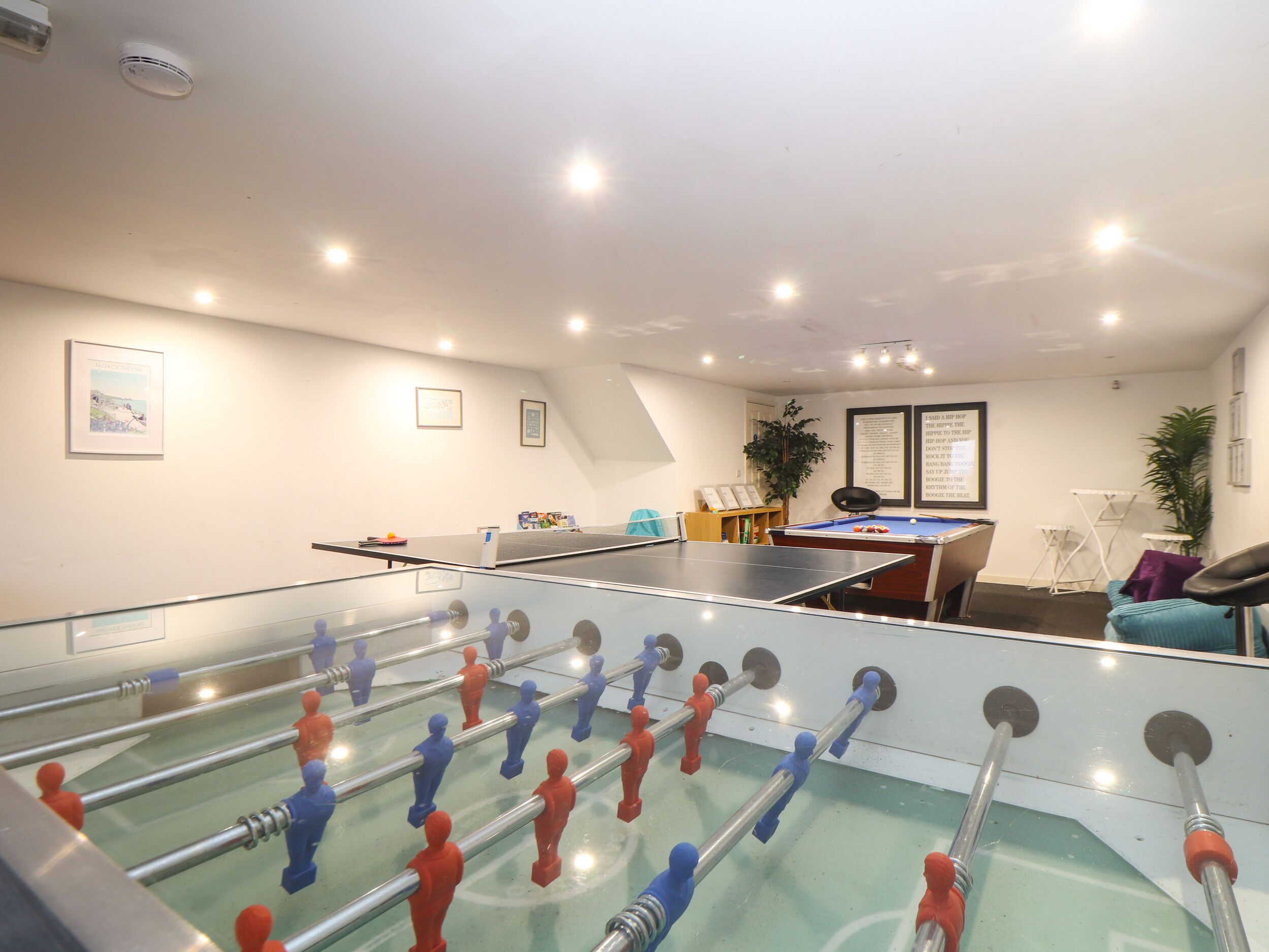 A room with a foosball table, a pool table, and a billiards table.