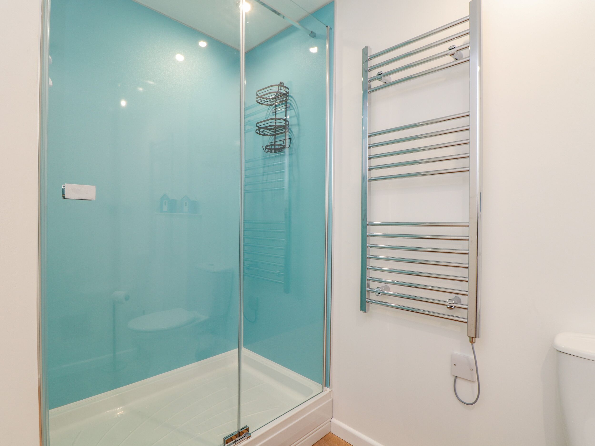 Een moderne badkamer met een douchecabine van glas, een glazen deur en een metalen handdoekrek.