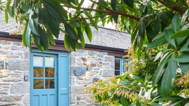 A stone building with a blue door and windows, surrounded by greenery. - Manacles (Falmouth)