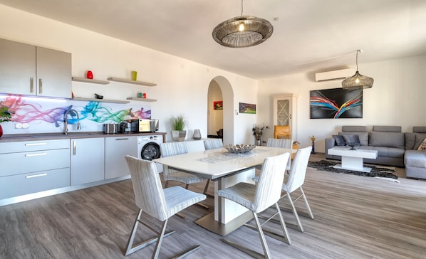 A modern kitchen with a dining area, a living room, and a hallway.