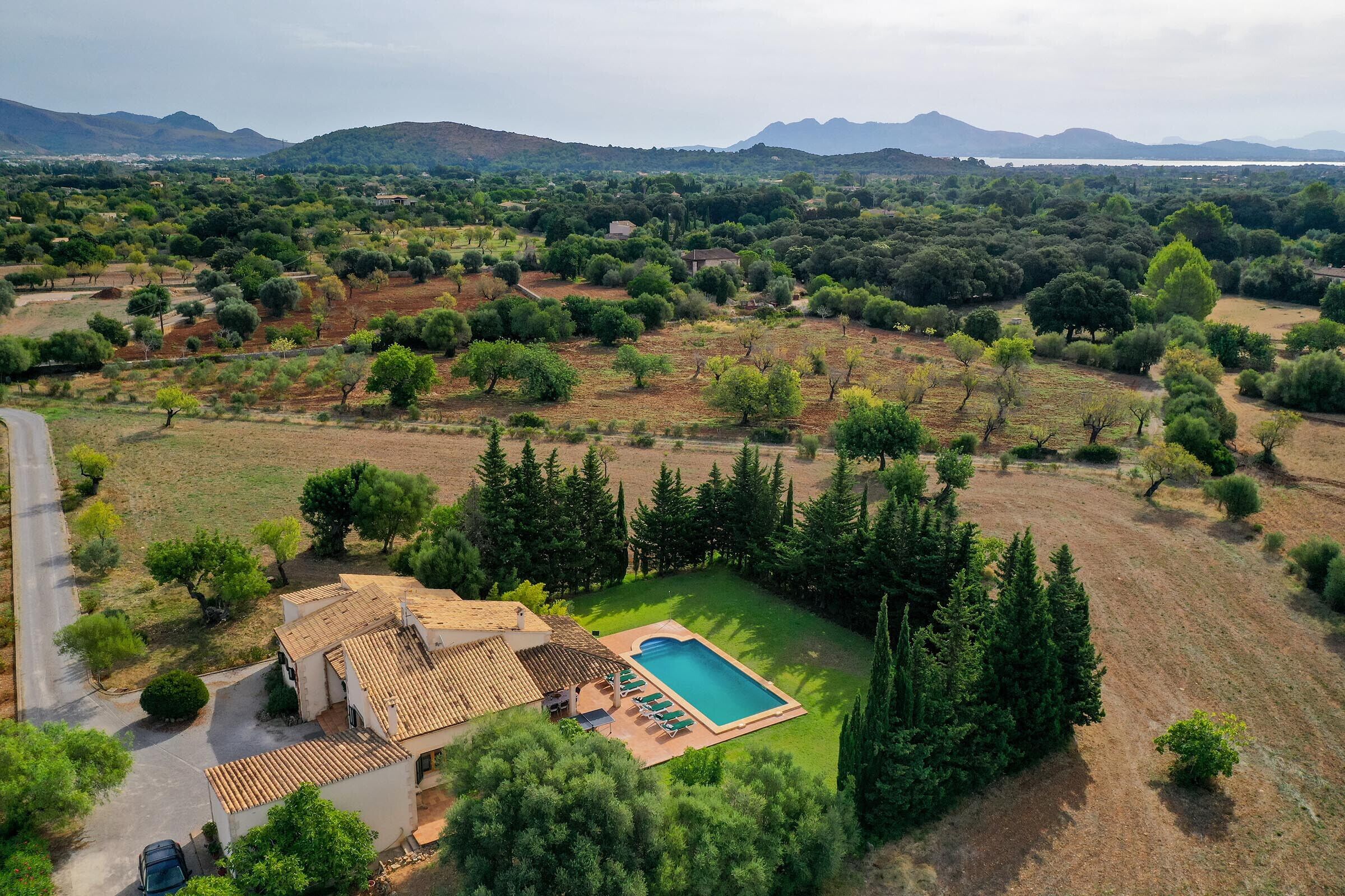 An aerial view of a property with a swimming pool, surrounded by trees and a hilly landscape.