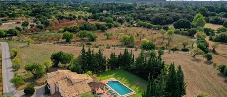 An aerial view of a property with a swimming pool, surrounded by trees and a hilly landscape.