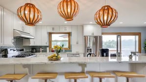 Une cuisine moderne avec des meubles blancs, un îlot central doté de tabourets et trois lampes suspendues.
