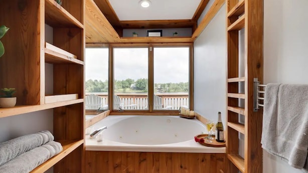 Une salle de bain moderne avec une baignoire sur pieds, des étagères en bois et une vue sur un balcon.
