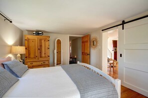 Un dormitori amb llit, armari de fusta i porta que dona a una altra habitació.