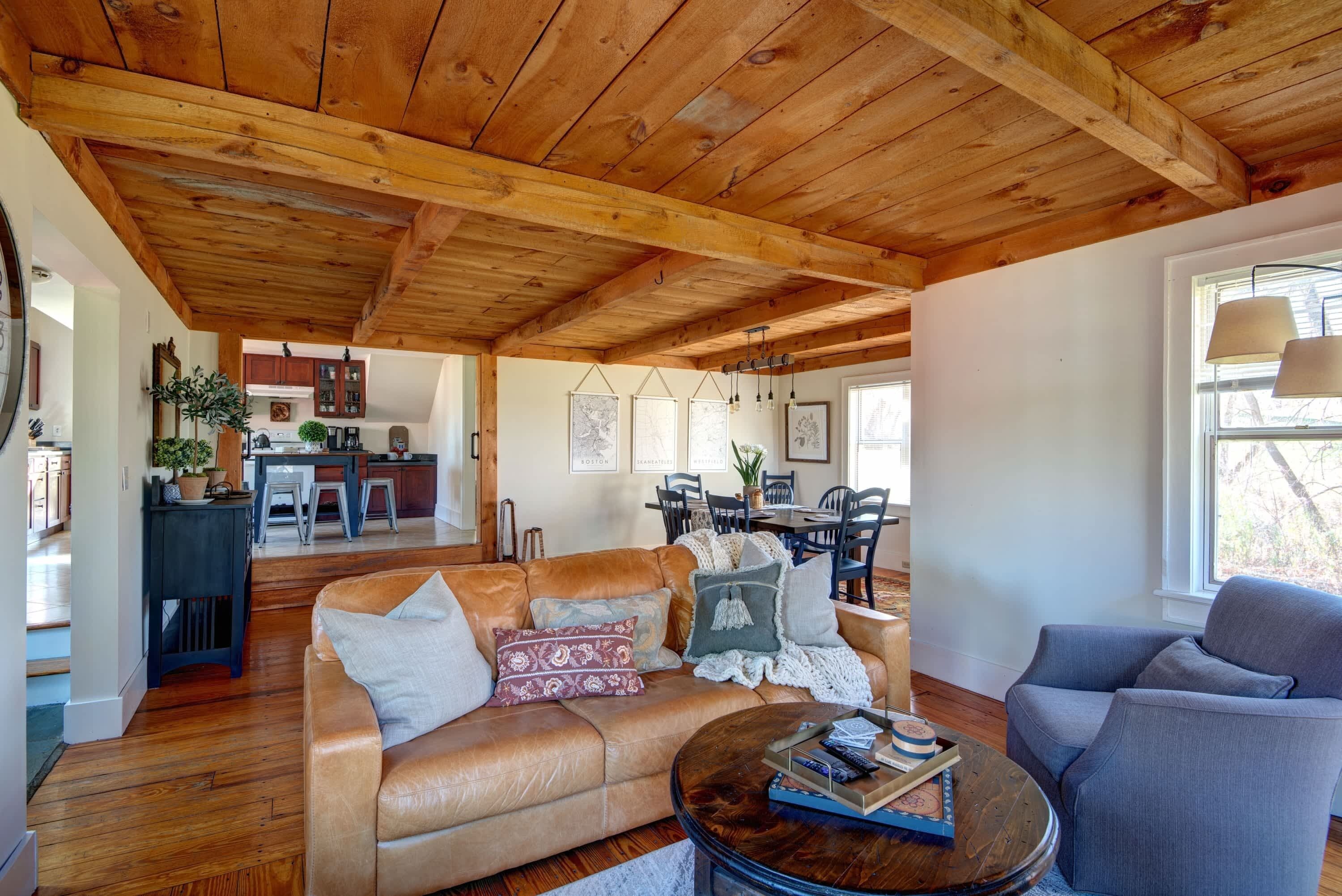 Un salon spacieux avec un plafond en bois, un canapé en cuir, un fauteuil bleu et un coin repas comprenant une table et des chaises.