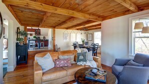 Amplia sala de estar con techo de madera, sofá de cuero, sillón azul y un comedor con mesa y sillas.