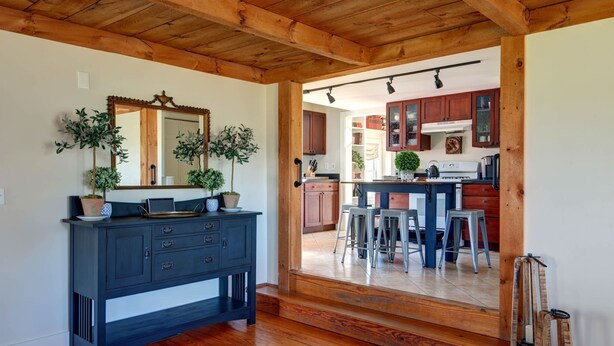 Techo de madera, cómoda azul oscuro y una cocina con armarios y taburetes de madera.