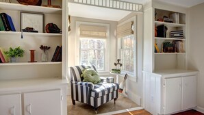 Una habitación con un sillón a rayas, una estantería y una ventana con persianas.