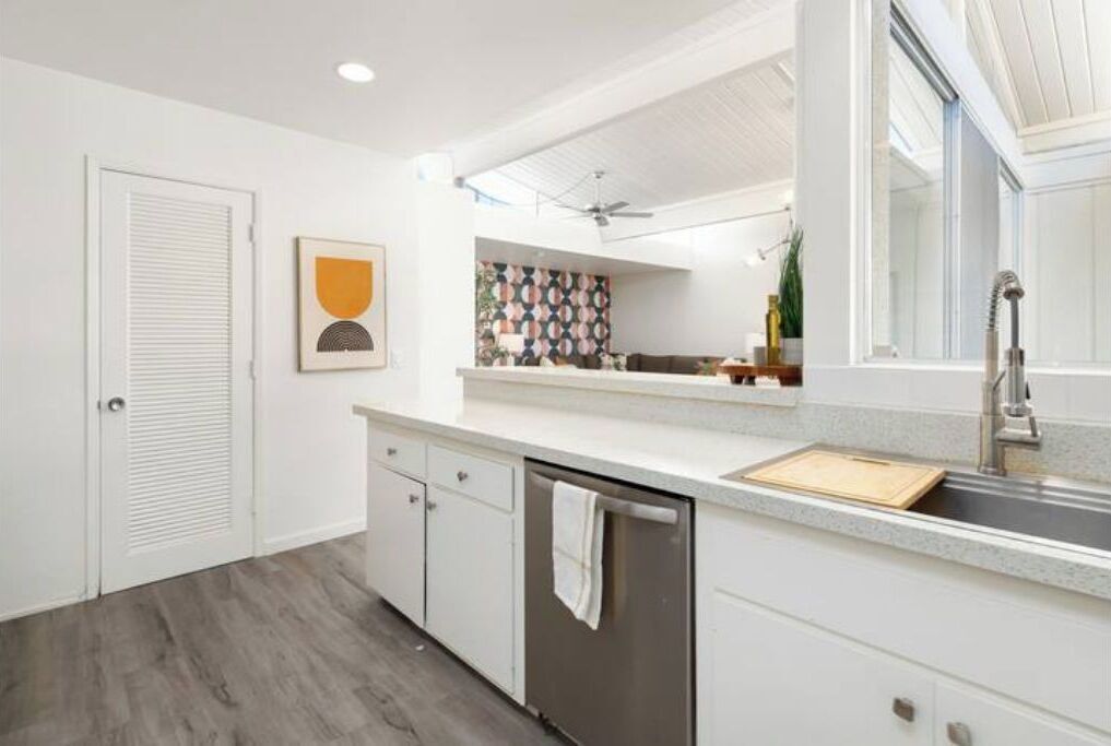 A modern kitchen with white cabinetry, a stainless steel dishwasher, and a large window providing natural light.
