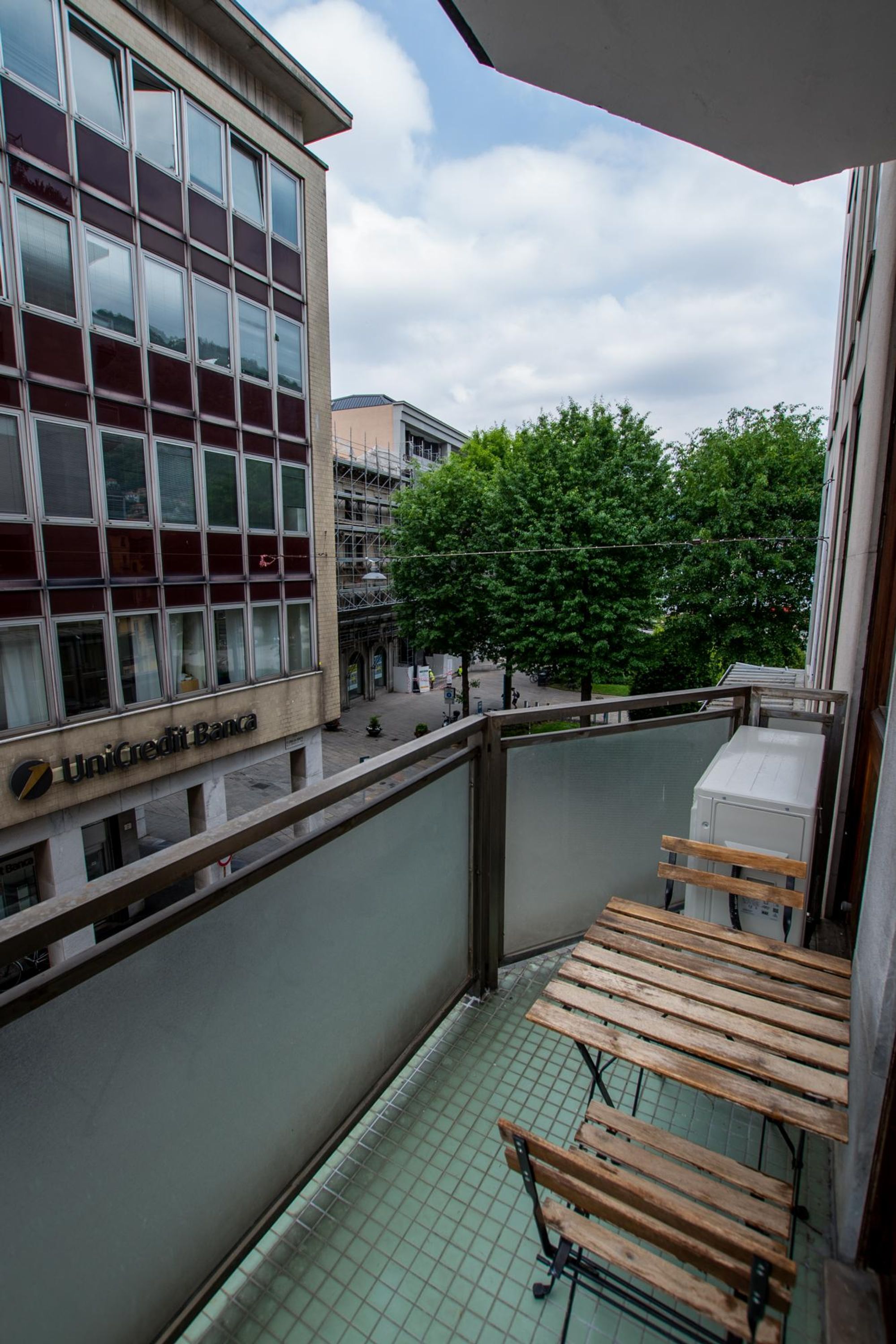 Un balcon d’où l’on aperçoit un bâtiment portant l’inscription « UniCredit Bank » et un arbre en arrière-plan.