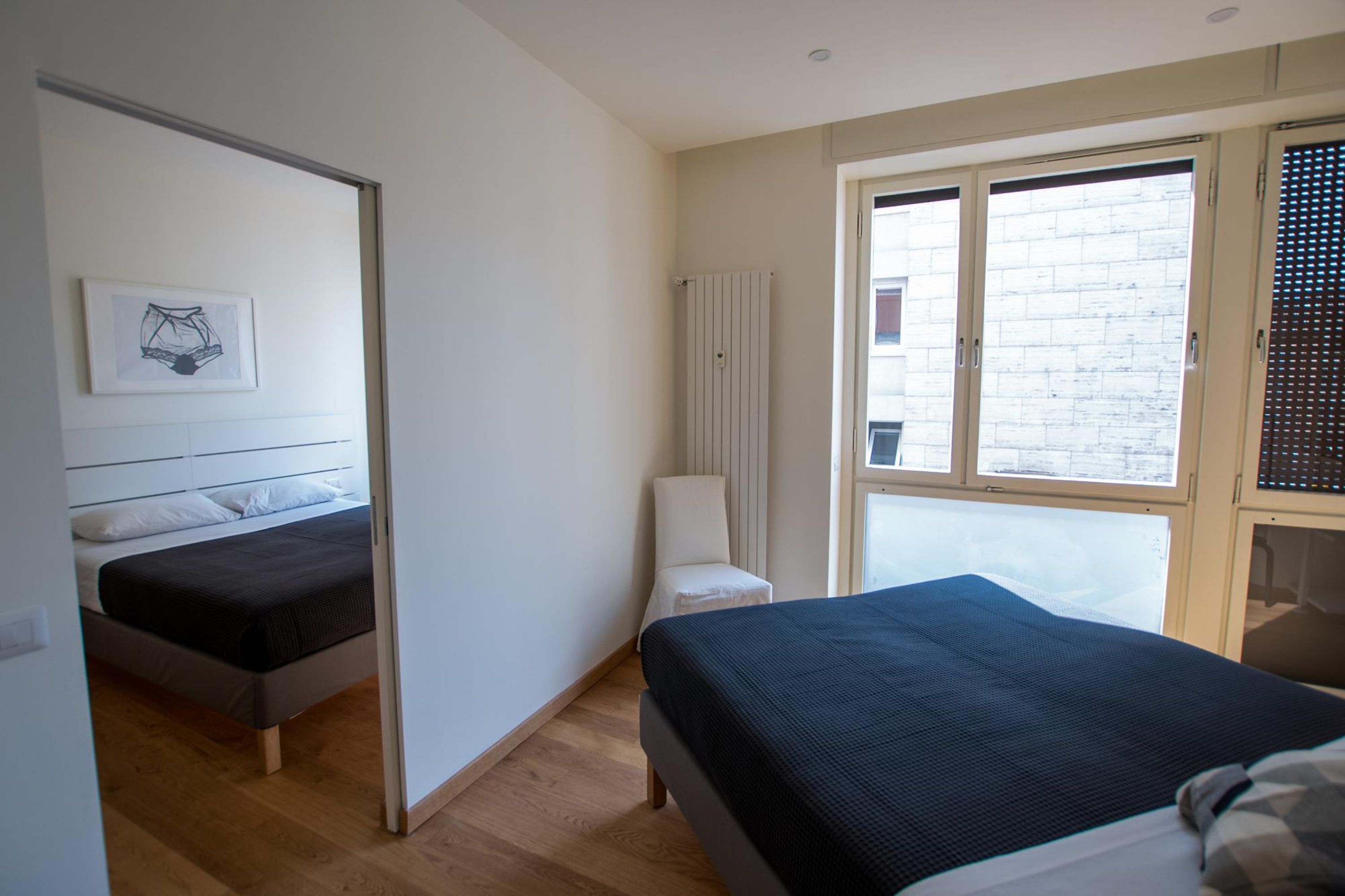 A bedroom with two beds, a radiator, a window with blinds, and a framed picture on the wall.