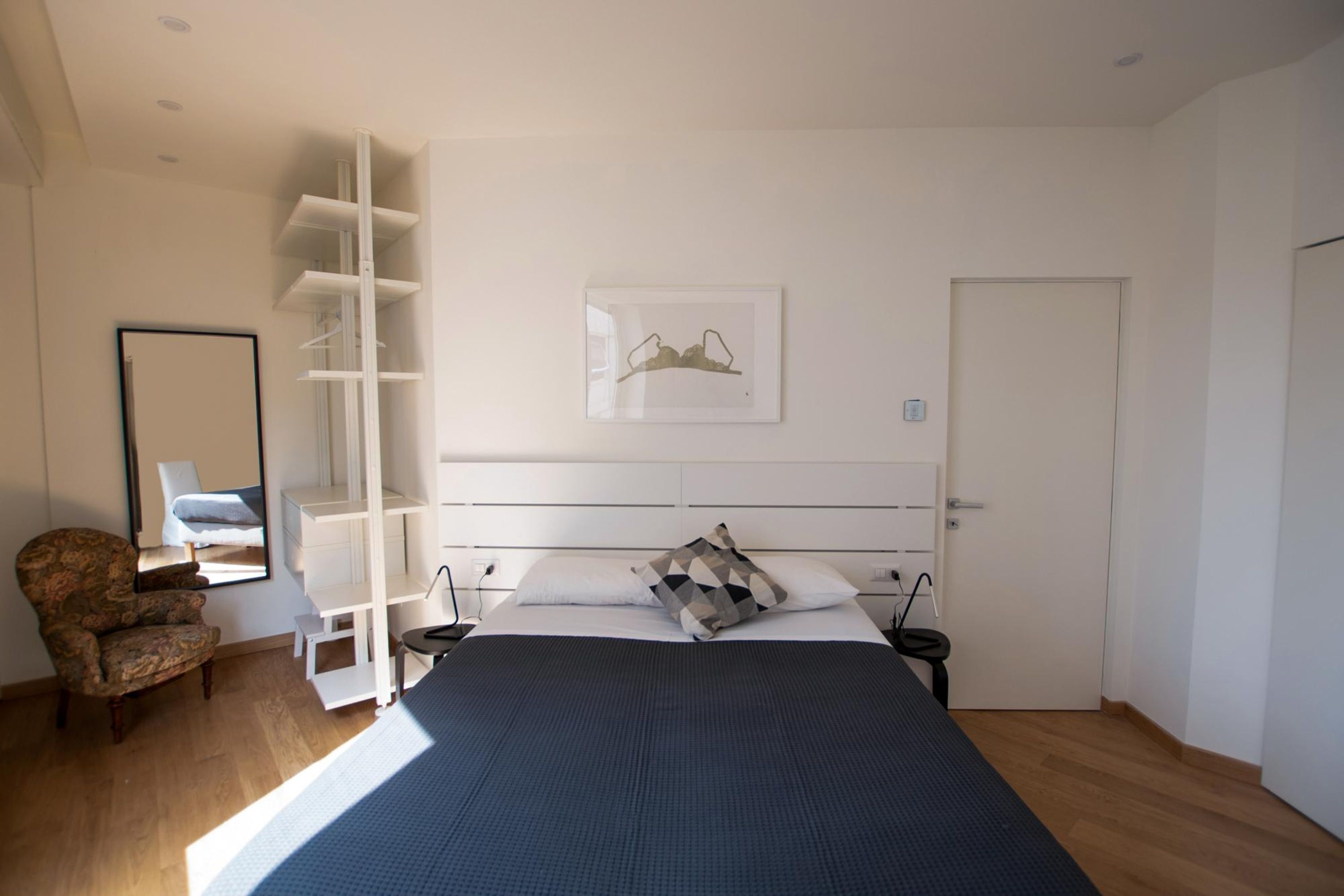Een slaapkamer met een bed, een stoel, een kledingkast en een lijst aan de muur.