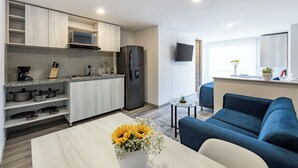 Una cocina moderna con microondas, estufa y refrigerador. Hay un comedor con una mesa y un sofá azul. Una mesita con una planta está cerca del sofá.
