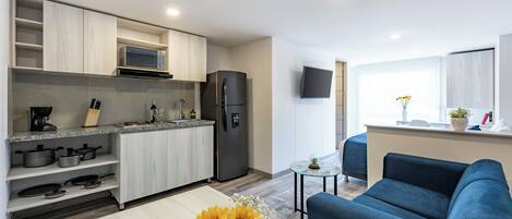 A modern kitchen with a microwave, stove, and refrigerator. There is a dining area with a table and a blue sofa. A small table with a plant is near the sofa.