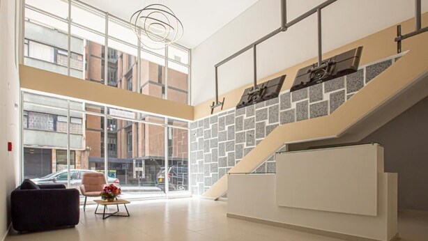 Un hall espacioso con techo alto, ventanas amplias, una escalera y una recepción.