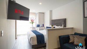 Una habitación de hotel moderna con cama, escritorio, televisor montado en la pared y zona de estar con sofá.