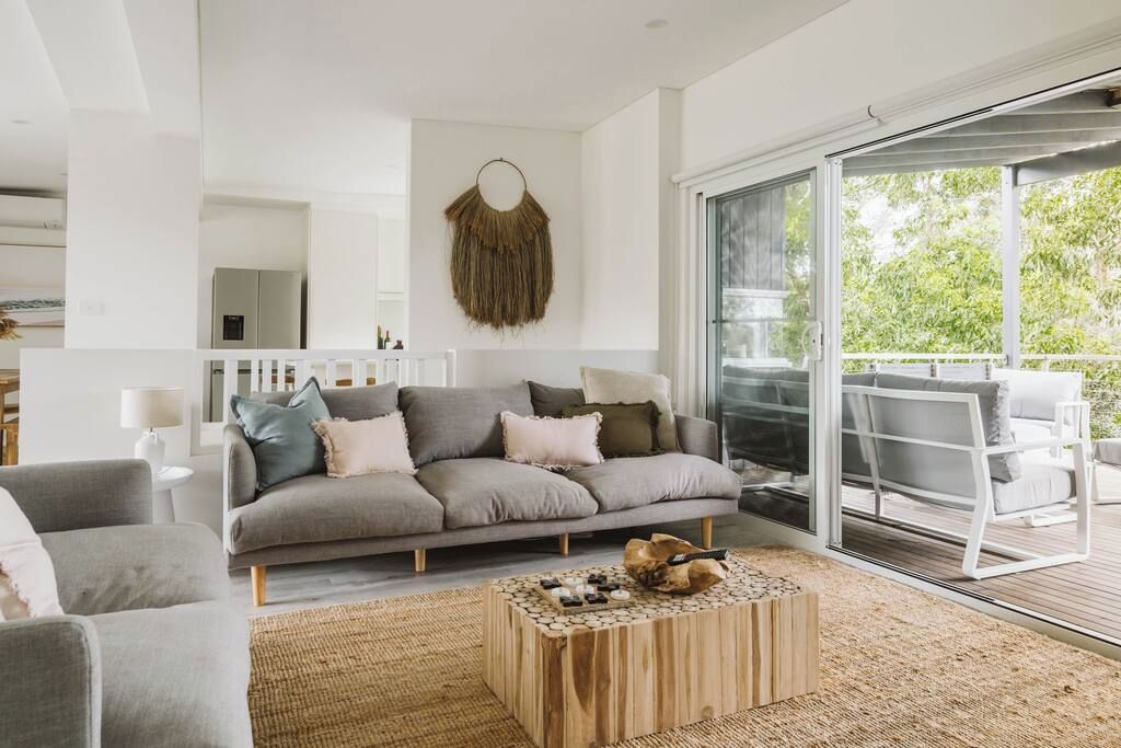 A modern living room with a grey sofa, a wooden coffee table, and a large sliding glass door leading to an outdoor area.