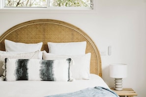 A bed with a woven headboard, white bedding, and a lamp on a bedside table. - Shoreline (Culburra Beach)